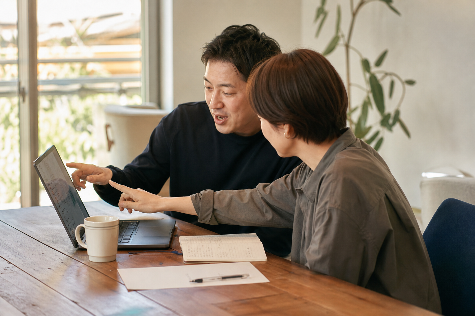 2人が同じノートPCの画面を一緒に指差しながらGA4の数字を確認している打ち合わせの一場面