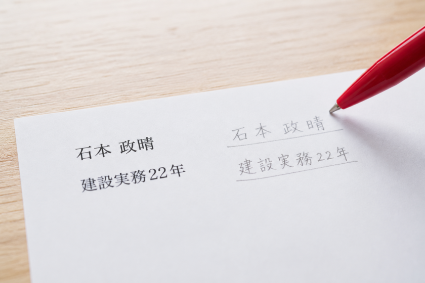 書類の氏名欄と年数欄に赤ペンの先が触れているマクロ接写