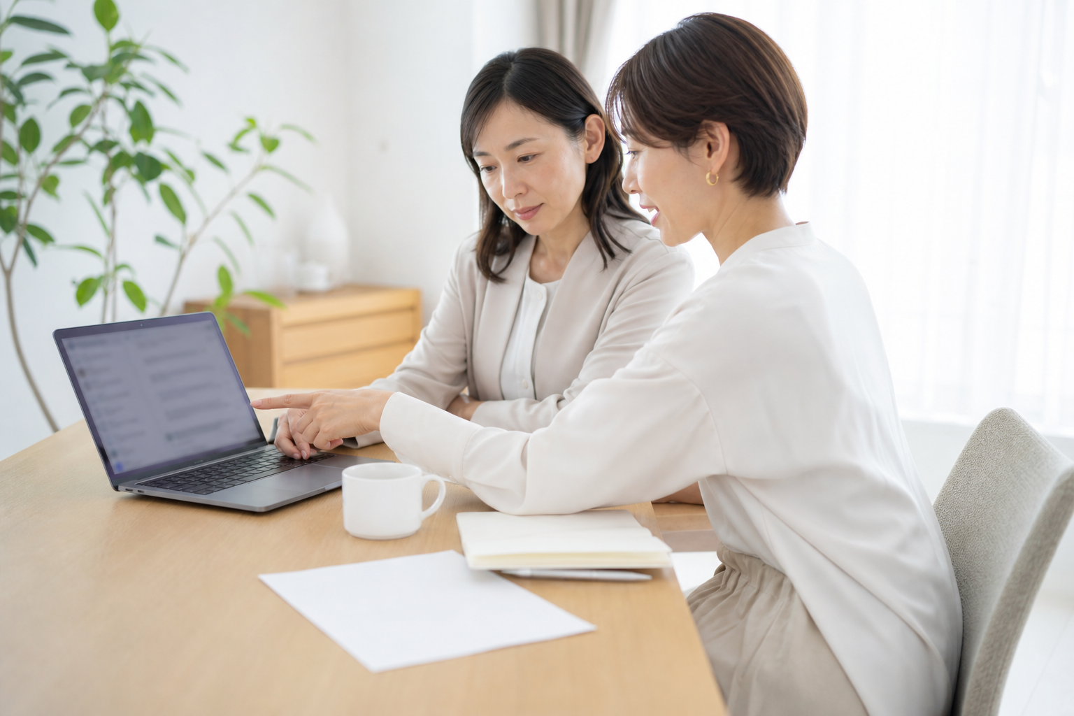 2人の担当者が同じノートPCでAI検索の結果画面を一緒に見ながら話し合っている打ち合わせの一場面